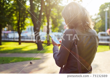 Mature business woman with smartphone. Sunny day in the city background 73132889
