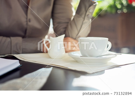 Coffee with milk, table in summer outdoor restaurant, business woman at table Coffee with milk, table in summer outdoor restaurant, business woman at table 73132894