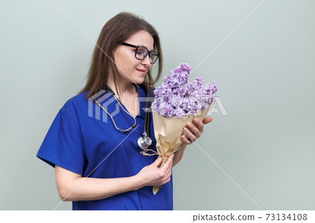 Doctor's Day, celebration. Happy smiling female medic with bouquet of flowers Doctor's Day, celebration. Happy smiling female medic with bouquet of flowers 73134108