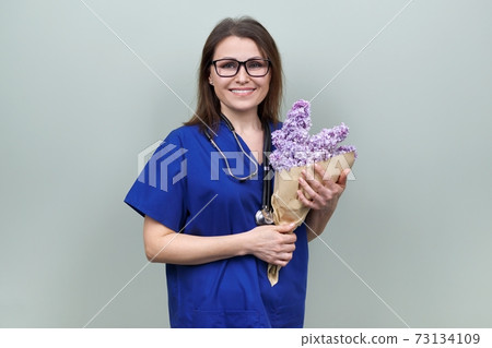 Doctor's Day, celebration. Happy smiling female medic with bouquet of flowers Doctor's Day, celebration. Happy smiling female medic with bouquet of flowers 73134109