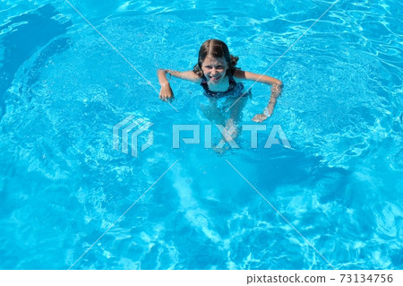 Kid has fun in an outdoor pool, child girl swims, dives, plays on the water, blue background Kid has fun in an outdoor pool, child girl swims, dives, plays on the water, blue background 73134756