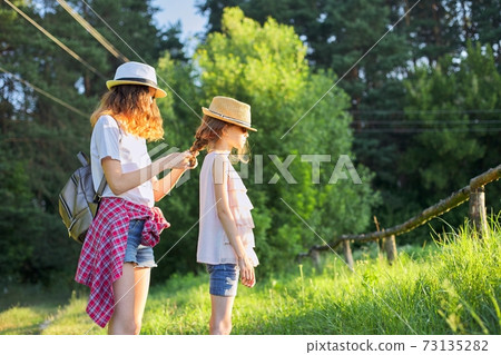 Summer, happy kids walking enjoying nature vacation, older sister braids her younger hair Summer, happy kids walking enjoying nature vacation, older sister braids her younger hair 73135282