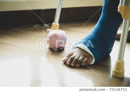 Man's leg uses crutches to walk after surgery recovery injury broken bones with a piggy bank 73136753