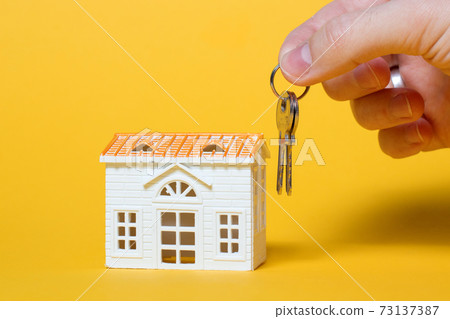 Small house with keys in hand on yellow background Small house with keys in hand on yellow background 73137387