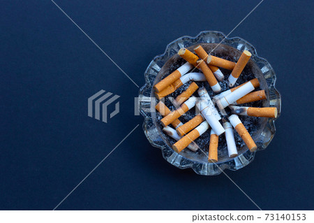 Cigarette butts in glass ashtray on dark background. Cigarette butts in glass ashtray on dark background. 73140153