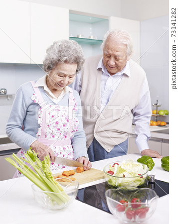 happy senior asian couple having a conversation while preparing meal together in kitchen 73141282
