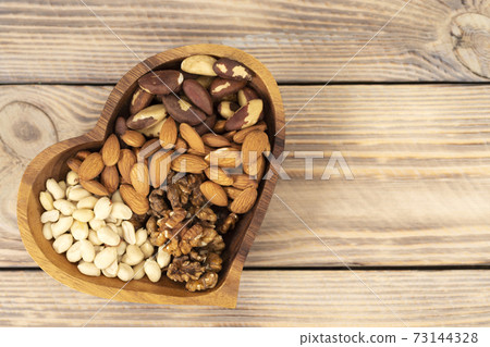 Natural nutritional blend of various nuts in a wooden plate in the shape of a heart symbol on a brown wooden table. A mixture of walnuts, brazil nuts, peanuts and almonds. Healthy natural food concept Natural nutritional blend of various nuts in a wooden plate in the shape of a heart symbol on a brown wooden table. A mixture of walnuts, brazil nuts, peanuts and almonds. Healthy natural food concept 73144328