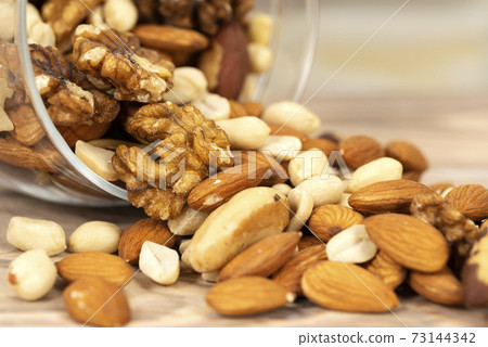 A mixture of different nuts is poured from a glass jar onto the table. Nuts as texture and background, macro A mixture of different nuts is poured from a glass jar onto the table. Nuts as texture and background, macro 73144342