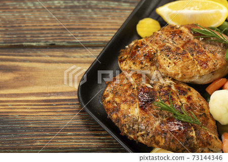 Grilled chicken breast in a skillet with vegetables and herbs, sliced lemon on a wooden board Grilled chicken breast in a skillet with vegetables and herbs, sliced lemon on a wooden board 73144346