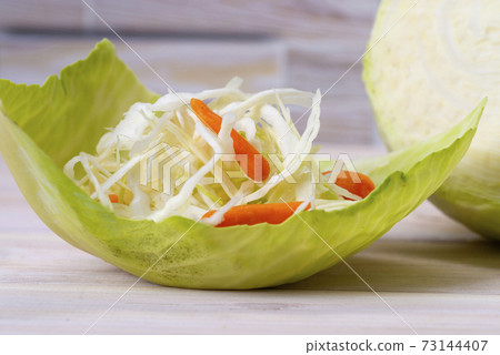 Fresh white cabbage and fresh cabbage salad with carrots with original serving on a cabbage leaf 73144407