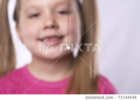 Little girl in pink holds a pulled out milk tooth on a thread 73144436