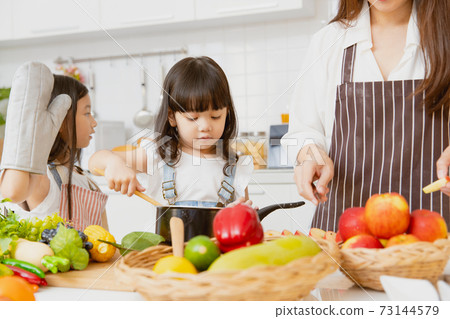 Little girl childs enjoy playing cooking with mom and older sister together at home kitchen holiday Little girl childs enjoy playing cooking with mom and older sister together at home kitchen holiday 73144579
