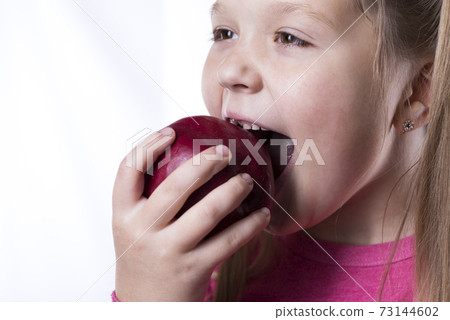 Little girl bites a red big apple on a white background, close-up 73144602