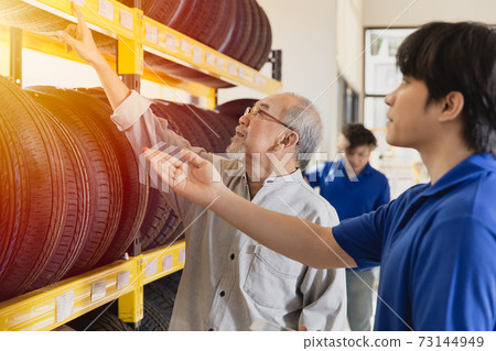 Customer selecting car tyres in garage and sale staff recommend various types of vehicle tires 73144949