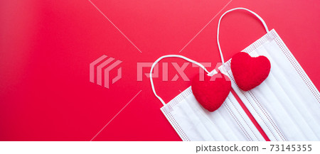 heart shape decoration and Medical face mask on red background against Coronavirus disease infection. Love, together and Happy Valentines day under Covid-19 pandemic concept 73145355