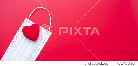 heart shape decoration and Medical face mask on red background against Coronavirus disease infection. Love, together and Happy Valentines day under Covid-19 pandemic concept 73145356