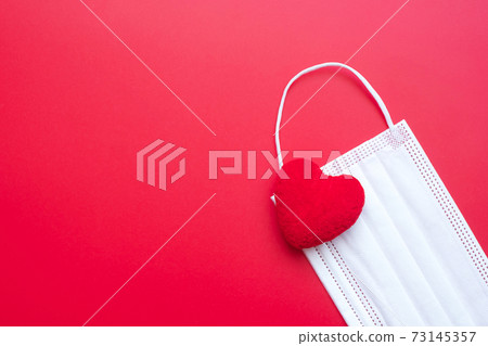 heart shape decoration and Medical face mask on red background against Coronavirus disease infection. Love, together and Happy Valentines day under Covid-19 pandemic concept heart shape decoration and Medical face mask on red background against Coronavirus disease infection. Love, together and Happy Valentines day under Covid-19 pandemic concept 73145357