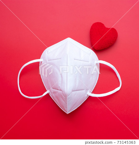 heart shape decoration and n95 Medical face mask on red background against Coronavirus disease infection. Love, together and Happy Valentines day under Covid-19 pandemic concept 73145363