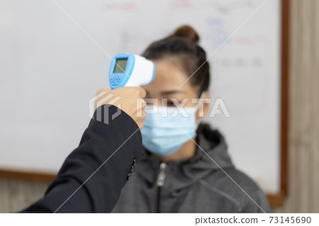 Teacher is taking a student's or college student's body temperature to measure the body of someone with a high fever and avoid the spread of the new flu, Welcome to the new student semester concept. 73145690