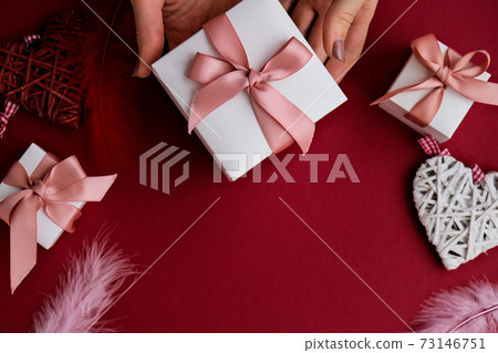 Flat lay of woman hands holding present with box decorated with pink ribbon on red background. Happy valentines day. Christmas Mother's Woman's Day 73146751