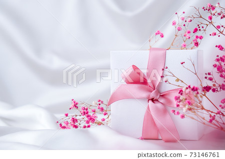 White present box with pink ribbon and small pink flowers on white silk fabric background. Greeting card for holidays. White present box with pink ribbon and small pink flowers on white silk fabric background. Greeting card for holidays. 73146761
