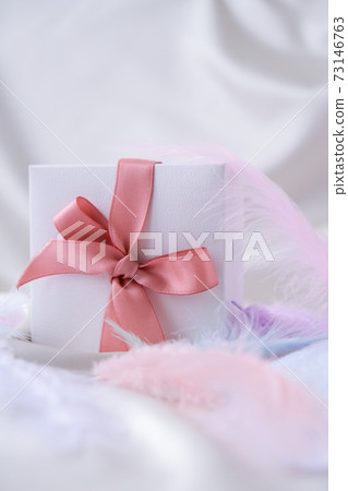 White gift box with pink ribbon on white silk texture background. Colorful bird feather. Holiday concept. White gift box with pink ribbon on white silk texture background. Colorful bird feather. Holiday concept. 73146763
