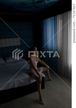 Seductive woman in lingerie sitting on bed 73147027