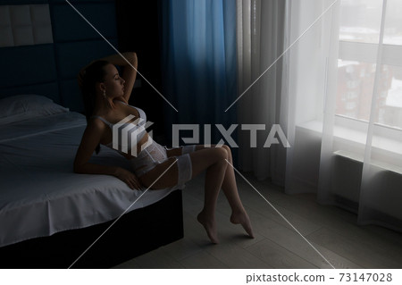 Seductive woman in lingerie sitting on bed 73147028