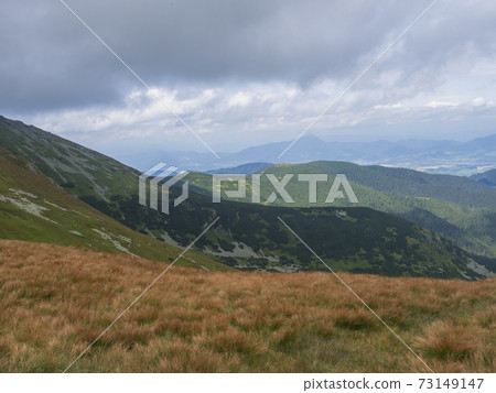 View from grassy hill slopes of hiking trail from Chopok at mountain meadow landscape of ridge Low Tatras mountains Nature park, Slovakia. cloudy late summer day View from grassy hill slopes of hiking trail from Chopok at mountain meadow landscape of ridge Low Tatras mountains Nature park, Slovakia. cloudy late summer day 73149147
