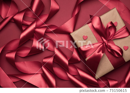gift box is packed in red paper and curled silk ribbon on a red background, festive background gift box is packed in red paper and curled silk ribbon on a red background, festive background 73150615