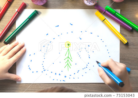 The child's hands draw a Christmas tree with markers on paper The child's hands draw a Christmas tree with markers on paper 73153043