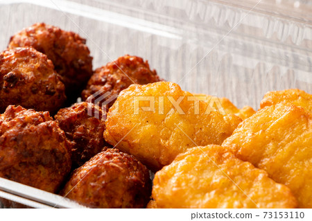 Takeout image. Deep-fried chicken nuggets and meatballs in a clear plastic container. 73153110