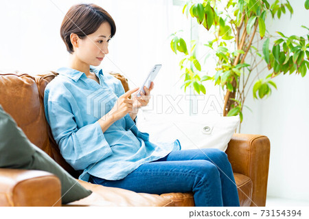 A woman using a smartphone on the sofa in the living room A woman using a smartphone on the sofa in the living room 73154394