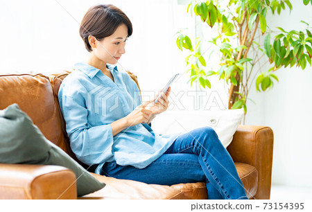 A woman using a smartphone on the sofa in the living room A woman using a smartphone on the sofa in the living room 73154395