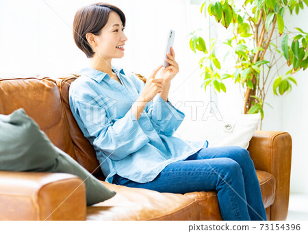 A woman using a smartphone on the sofa in the living room A woman using a smartphone on the sofa in the living room 73154396