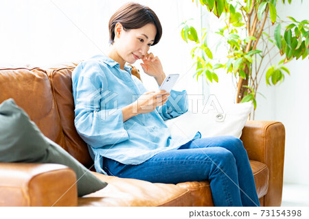 A woman using a smartphone on the sofa in the living room 73154398