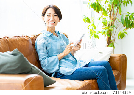 A woman using a smartphone on the sofa in the living room 73154399