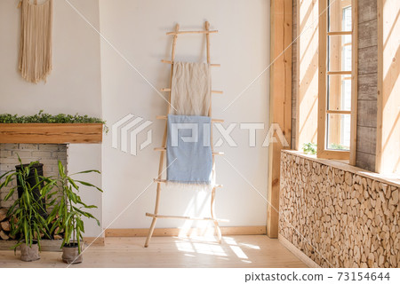 Cozy sunny room in light colors with wooden floor and walls, fireplace and green plants in pots. Scandinavian simplicity design. Eco loft apartments. Cozy sunny room in light colors with wooden floor and walls, fireplace and green plants in pots. Scandinavian simplicity design. Eco loft apartments. 73154644