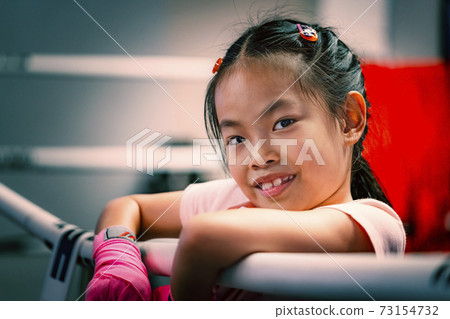 Portrait Asian child girl on boxing ring, holding boxing ring's robe, close up to cute face with smile, eyes looking at camera, adjusted colour. Child girl practices self-defence, Thai boxing. Portrait Asian child girl on boxing ring, holding boxing ring's robe, close up to cute face with smile, eyes looking at camera, adjusted colour. Child girl practices self-defence, Thai boxing. 73154732