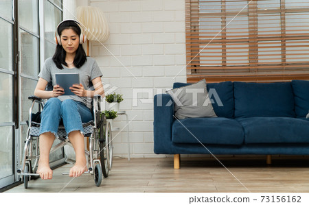 Happy disabled Asian woman sitting in a wheelchair And working with tablet at home, The concept of Technologies for the convenience of people with disabilities. 73156162