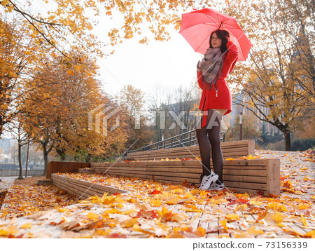 young girl in a red coat with an umbrella standing on the alley young girl in a red coat with an umbrella standing on the alley 73156339