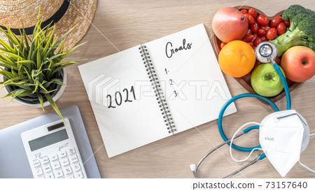 2021 goals on note book for new year list reminder in notebook of yearly planner and health plan for work-life balance on desk background of computer, healthy food, face mask for covid-19 protection 73157640