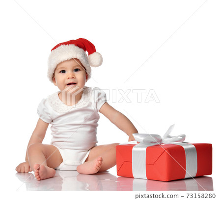 Infant baby girl child in red Santa hat with gift Infant baby girl child in red Santa hat with gift 73158280