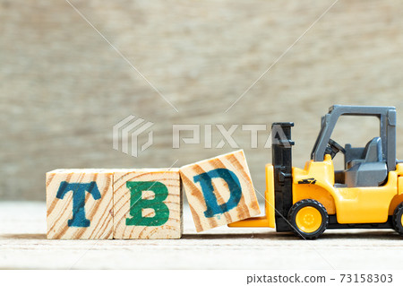 Toy forklift hold letter block d to complete word TBD (Abbreviation of to be defined, discussed, determined, decided, deleted or declared) on wood background 73158303