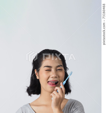 Dental brace teenager girl smile holding toothbrush and looking to camera. white teeth with blue braces. Dental care. Asian woman with contact lens and orthodontic accessories. Cosmetic dentistry. 73160468
