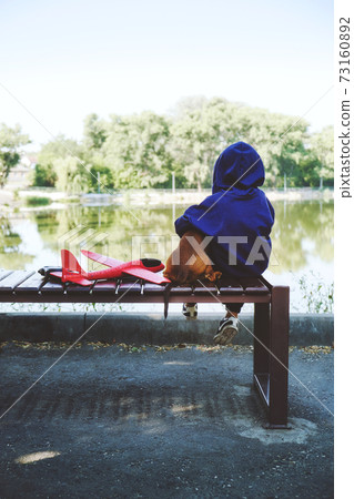 Sad kid sitting alone with dog and toy airplane on bench by the river bank. Diagnosing Early-Onset Childhood depression, autism 73160892