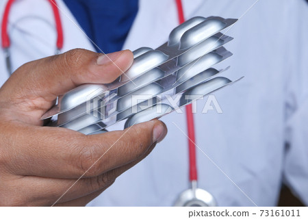 doctor hand in protective glass holding blister pack  73161011
