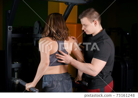 The trainer helps the girl do the triceps exercise. The trainer helps the girl do the triceps exercise. 73161248