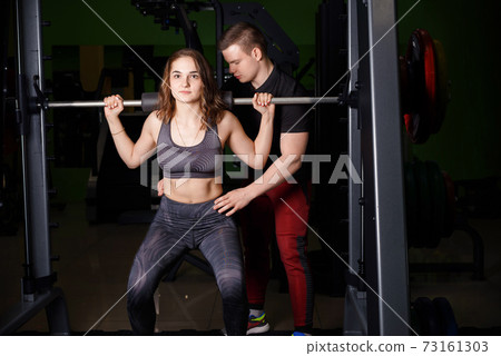 The trainer helps the girl to perform the exercise on the Schmitt simulator. 73161303