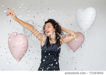 The emotion of success. Happy sexy brunette girl enjoying celebrating with confetti and heart balloons on a white background 73163692